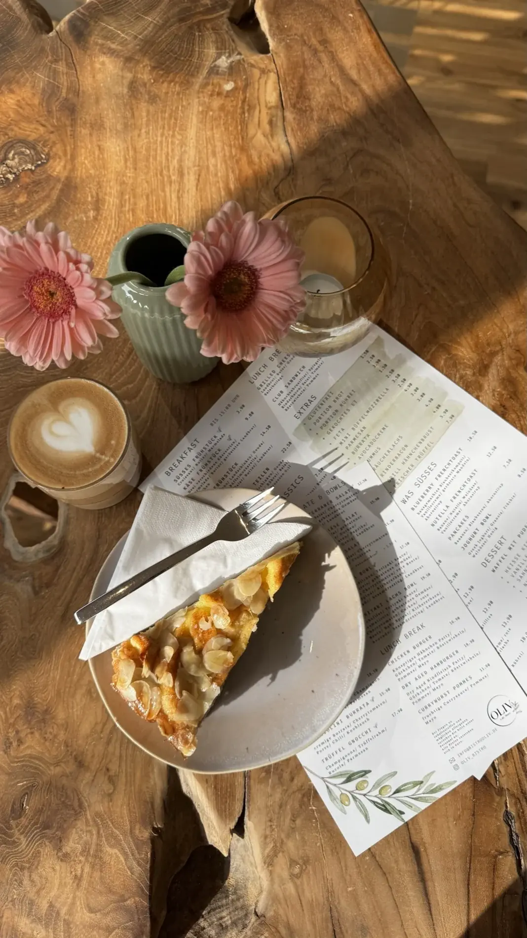 Kuchen und Cappuccino neben rosa Blumen im Sonnenlicht